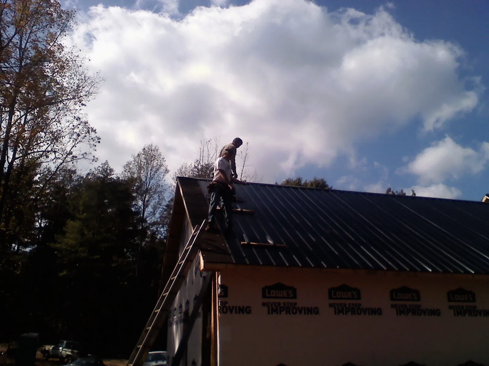 Roofer fastening dark metal panels high against a cloudy sky, from a Roof Inspection job in Varnville