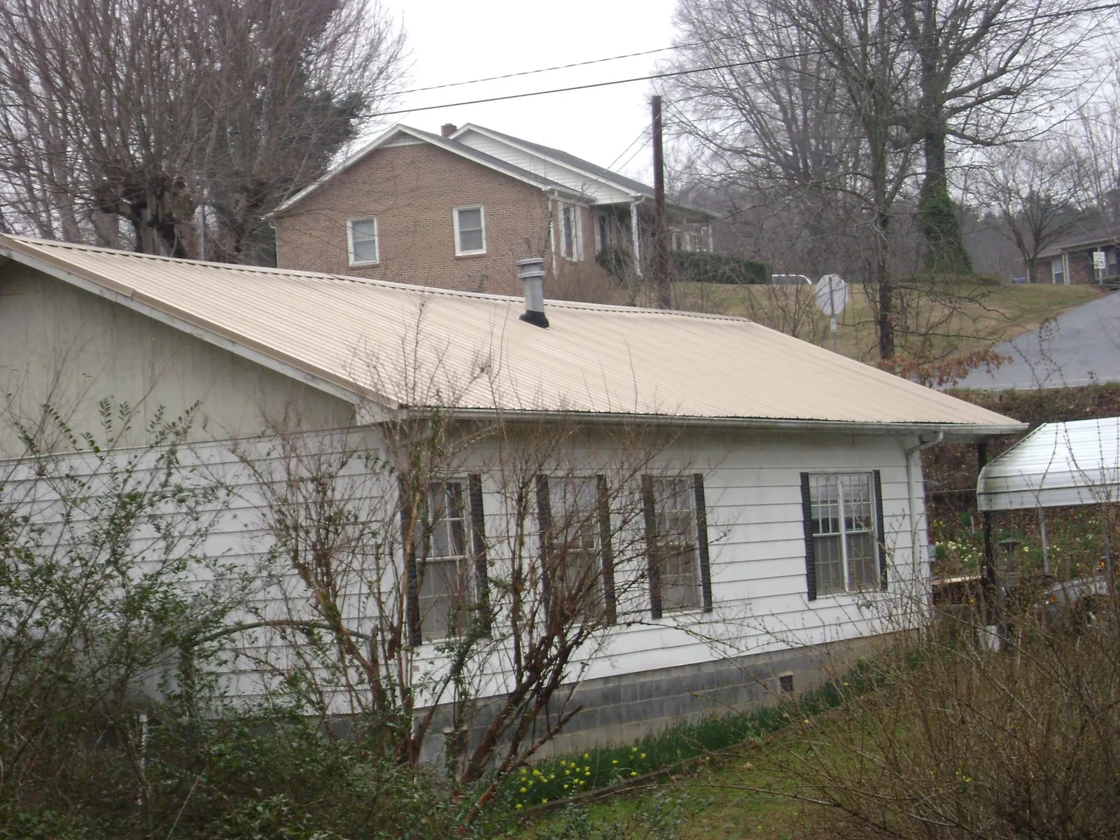 Tan metal roof on a white sided house set into a hillside — Commercial Roofing by Roofing Brothers in Varnville